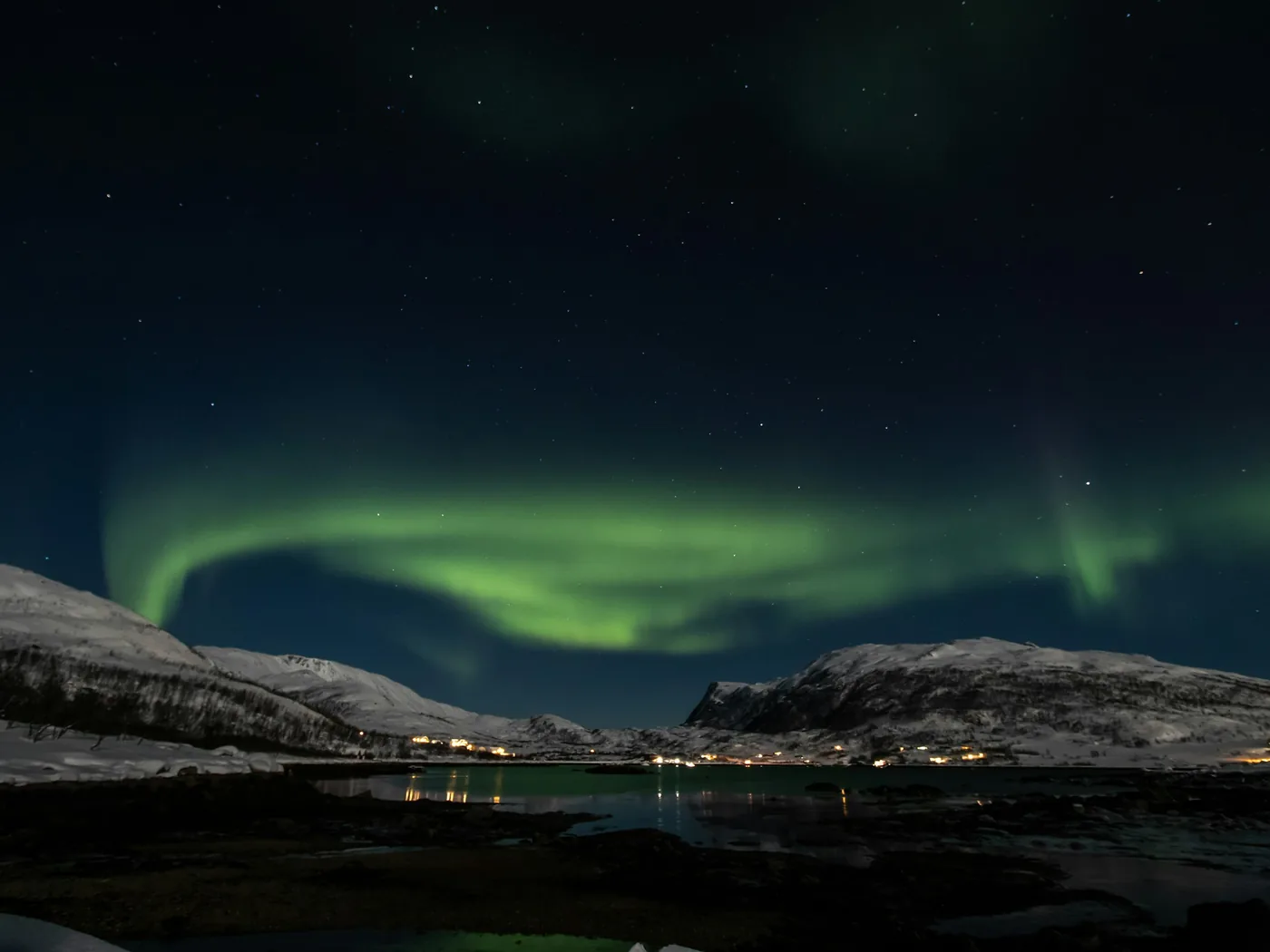 Bright green aurora curtains reflected in a still Arctic fjord