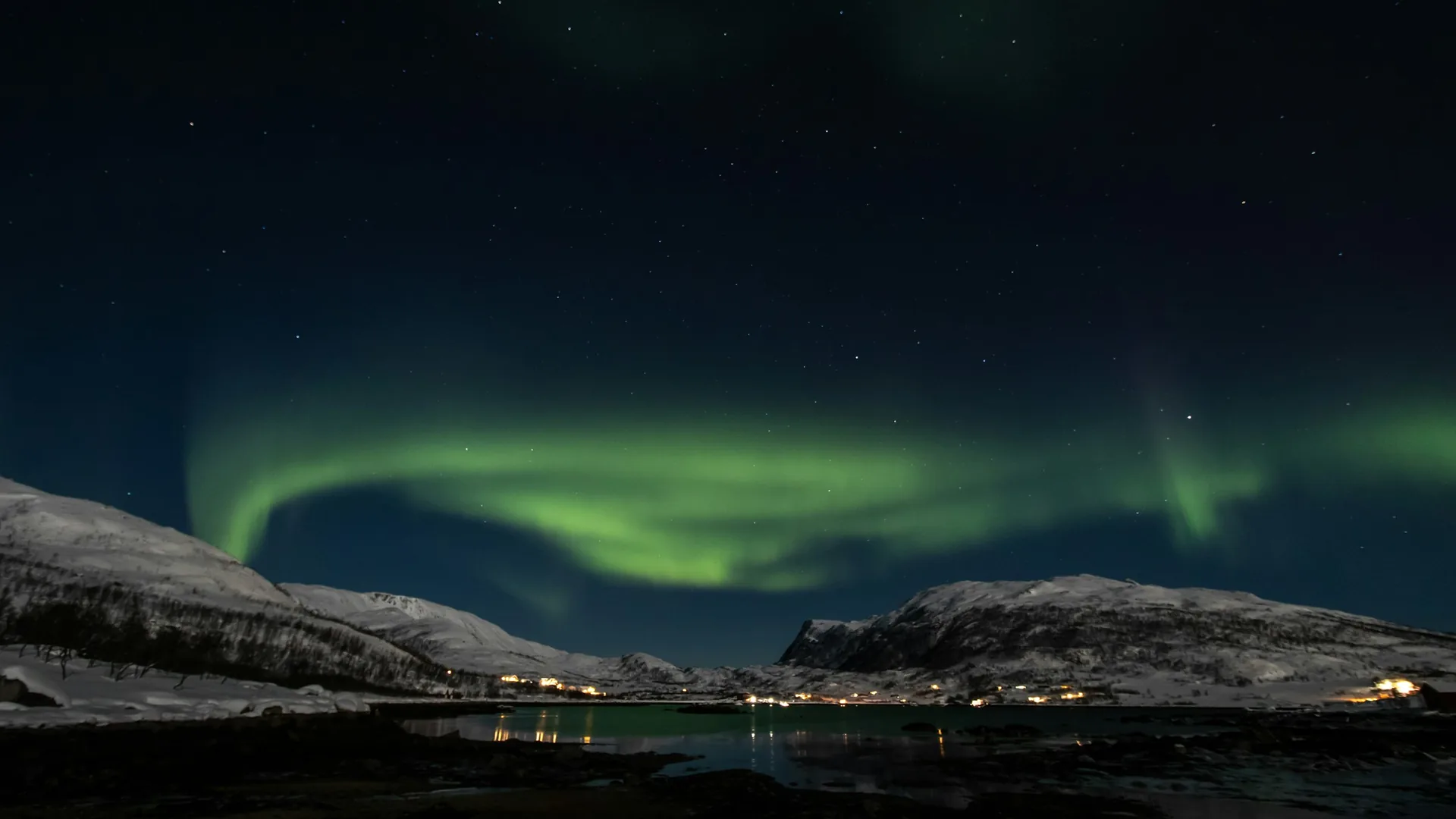 Green aurora borealis swirling over a snowy fjord landscape near Tromsø, Norway